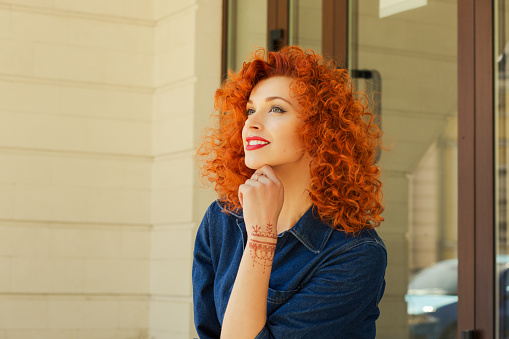 Thinking about new job new life. Beautiful red head curly woman person girl looking up thinking about future boyfriend family deciding what to do isolated outdoor street apartment complex background