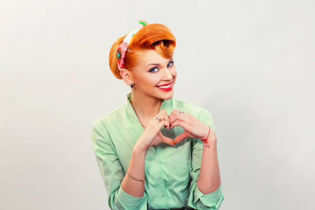 Closeup red head young woman pretty pinup girl green button shirt giving thumbs up sign gesture looking at you camera isolated white background retro vintage 50's style. Human emotions body language Closeup portrait smiling cheerful happy young pin up woman making heart sign with hands isolated grey wall background. Positive human emotion expression feeling life perception attitude body language pin up girl photos stock pictures, royalty-free photos & images