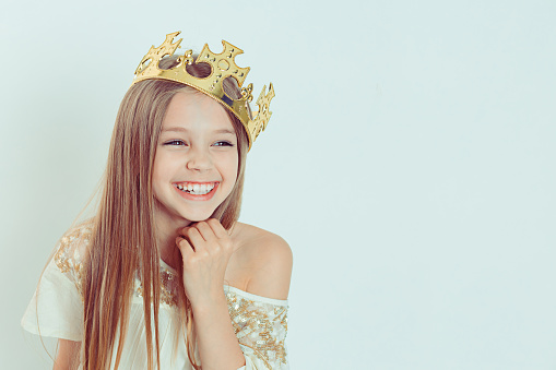 Mini Miss. Young happy girl with a cute smiling laughing wearing a crown and a white dress on Holiday looking side wards isolated green background