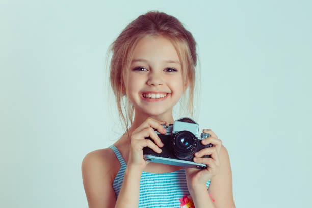 beautiful smiling happy child (kid, girl) holding taking pictures looking at you camera gesture - bellow camera photography photography themes photographer imagens e fotografias de stock