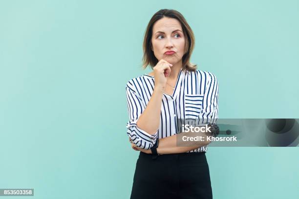 Thoughtful Business Woman Looking Away While Standing Against Light Blue Wall Stock Photo - Download Image Now