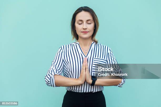 Meditation Religion And Spiritual Practises Beautiful Business Woman Doing Yoga Indoors At Light Blue Wall Keeping Eyes Closed Holding Fingers In Mudra Gesture Stock Photo - Download Image Now