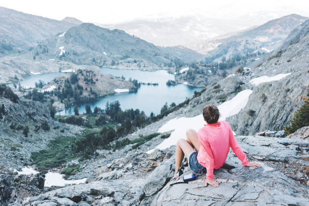 Brave woman resting high in mountains. Risky rock climbing in peaceful wilderness area. Enjoying amazing snowy lake view