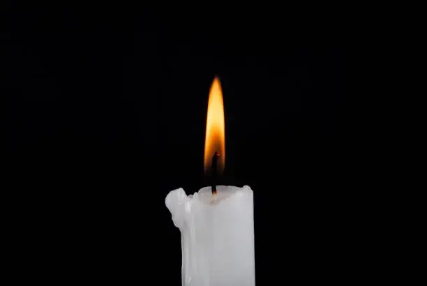 Photo of White paraffin candle burning isolated on black background. Close up