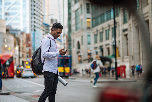 Indian young man in London, crossing the busy street while multi tasking