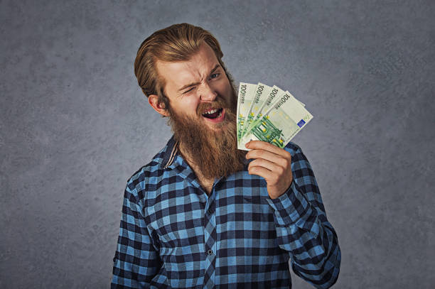 Portrait happy man blinking eye ecstatic celebrates success holding in hand euro bills banknotes isolated gray background with copy space. Financial freedom concept stock photo