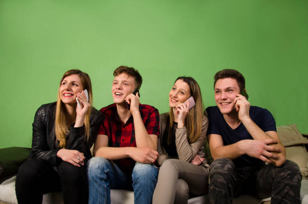 Group of four young people, two teens and two young adults talking on smartphone in the same time while sitting on the couch