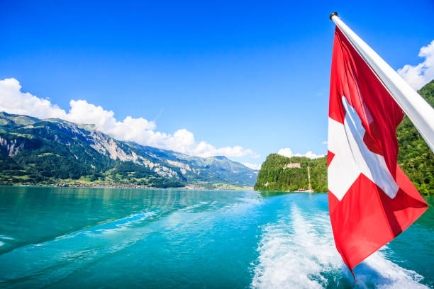 switzerland national flag at cruise boat's rear end with beautiful summer view of swiss natural alps, lake and clear blue sky as a background, lake brienz, interlaken-oberhasil, bern, switzerland. - interlaken berne brienz lake imagens e fotografias de stock