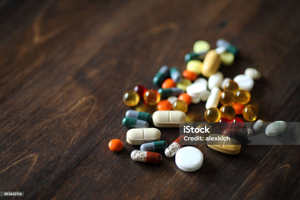 Medications and tablets on a wooden texture table Different colored medications and tablets on a wooden texture table Capsule - Medicine Stock Photo