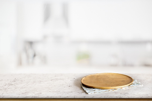 Empty round wooden plate or wooden dish on marble counter in blurred kitchen background. For food and product display montage.