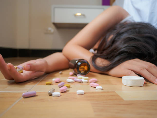young woman is lying on the floor with a lot of pills. overdose and suicide concept. - alcoholism narcotic excess alcohol imagens e fotografias de stock