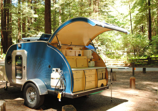 A blue teardrop camping trailer is setup at a campsite surrounded by redwood trees in Humboldt Redwoods State Park in California