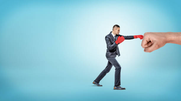 赤いボクシング グローブの小さいビジネスマンは、青の背景に巨大な男性の拳をパンチします。 - business team corporate business business person ストックフォトと画像