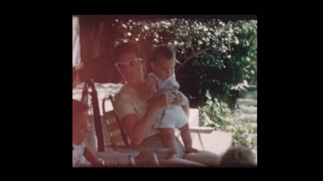 1960 mother and baby boy hanging out with family in backyard