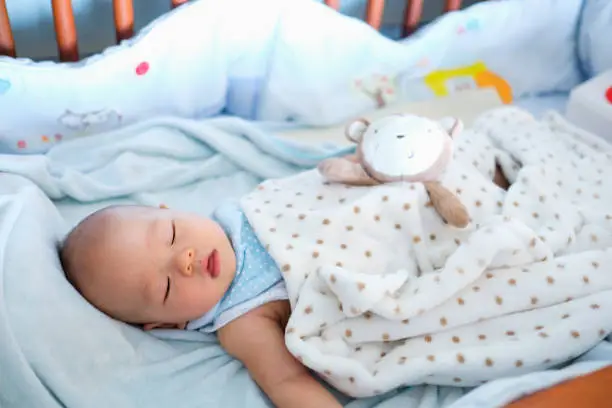 Photo of Cute little Asian 6 months old  baby boy child sleeping in baby cot / crib in bedroom, Peaceful kid lying on baby bed while sleeping, Daytime sleep concept / Selective focus