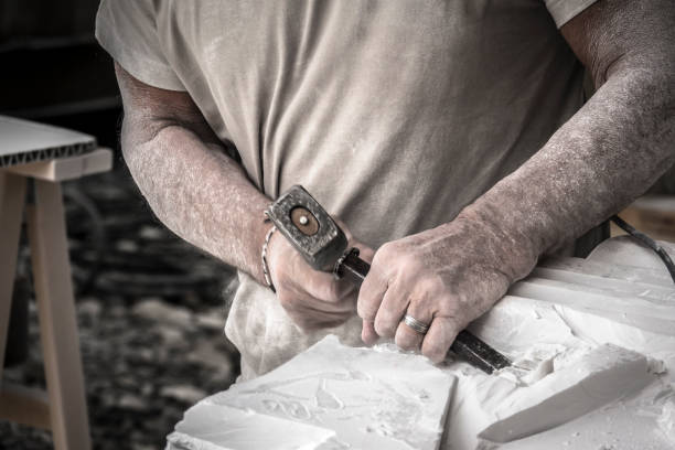 Detail of artist's hands sculpting marble with hammer and chisel stock photo