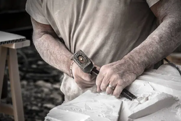 Photo of Detail of artist's hands sculpting marble with hammer and chisel