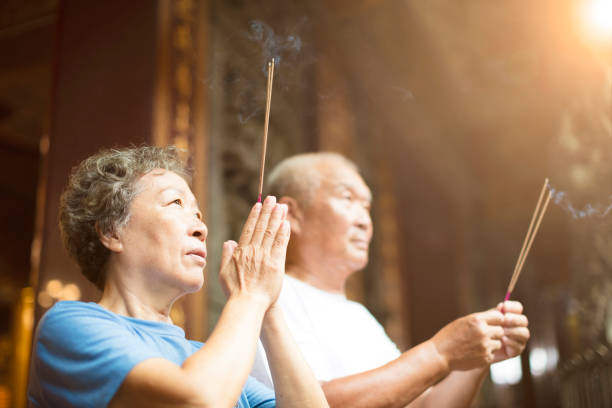 senior couple praying buddha with incense stick at temple - burning incense imagens e fotografias de stock