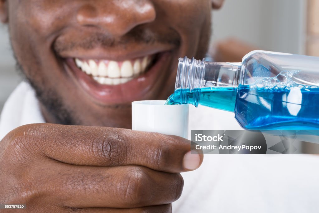 Close-up Of A Man Pouring Mouthwash Into Cap Close-up Of A Smiling African Man Pouring Mouthwash Into Cap Mouthwash Stock Photo