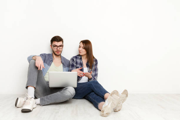 istock Couple web-surfing with laptop in empty room 853760482