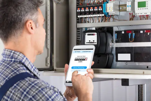 Close-up Of A Male Technician Doing Meter Reading Using Mobilephone