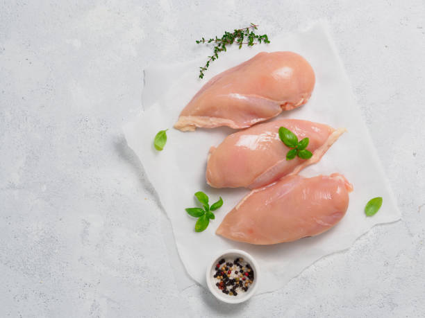istock Raw chicken breast with fresh basil on paper over gray cement background 853788704