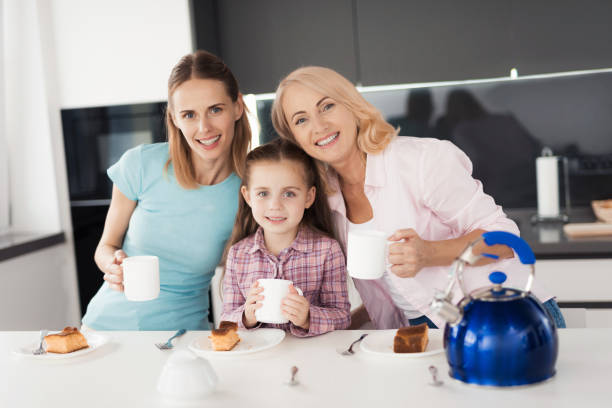 rodzina pozuje w kuchni z filiżankami herbaty w rękach. patrzą na kamerę i uśmiechają się. - grandmother pie cooking baking zdjęcia i obrazy z banku zdjęć