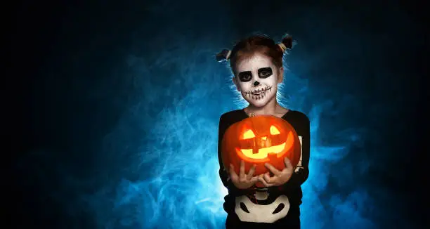 Photo of magic skeleton with  pumpkin. baby girl in costume to halloween