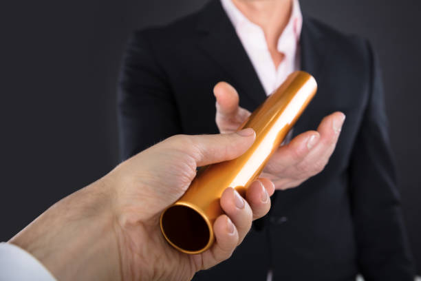 Businessman Passing A Golden Relay Baton Close-up Of A Businessman Passing Golden Relay Baton To Colleague continuity stock pictures, royalty-free photos & images