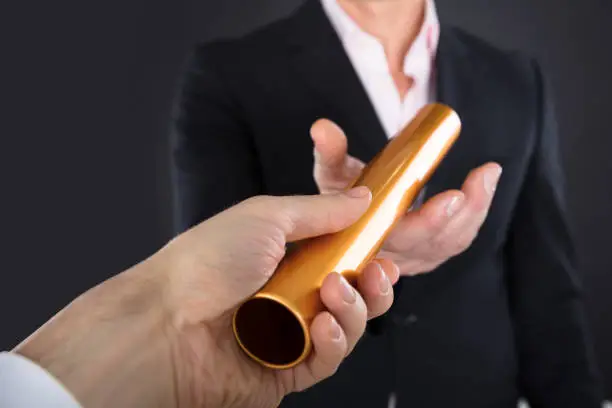 Close-up Of A Businessman Passing Golden Relay Baton To Colleague