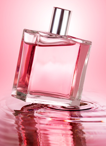 perfume bottle over rippled water isolated on pink background