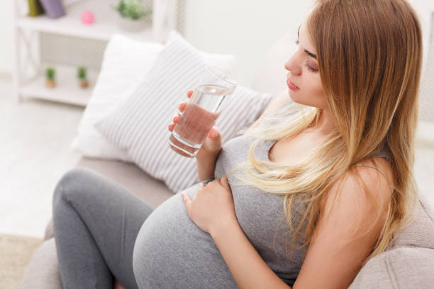 クローズ アップのソファの上に座って水のガラスと妊娠中の女性 - water women glass healthy eating ストックフォトと画像