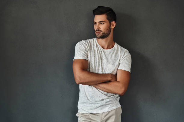 Too good to be real. Handsome young man looking away and keeping arms crossed while standing against grey background sex symbol stock pictures, royalty-free photos & images