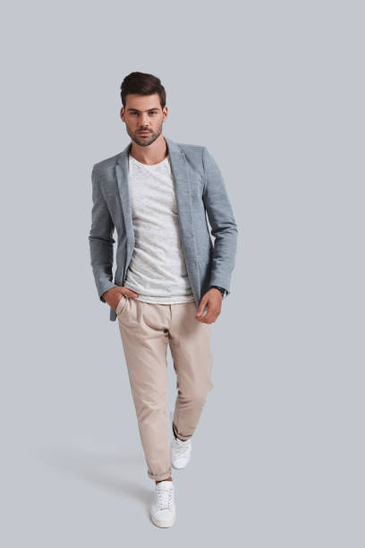 Confident in his style. Full length of good looking young man keeping hand in pocket and looking at camera while walking against grey background preppy fashion stock pictures, royalty-free photos & images