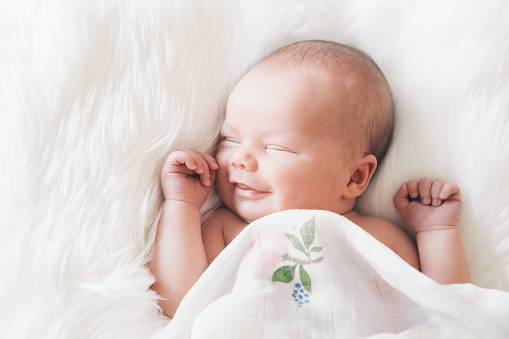 Laughing, morning and portrait of a baby on a bed to wake up, relax and play. Smile, cute and a child in the bedroom after a nap, sleeping or rest for comfort, relaxing or happiness while playing