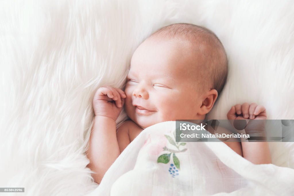 Sleeping newborn baby in a wrap on white blanket. Sleeping newborn baby in a wrap on white blanket. Beautiful portrait of little child girl 7 days, one week old. Baby smiling in a dream. Baby - Human Age Stock Photo