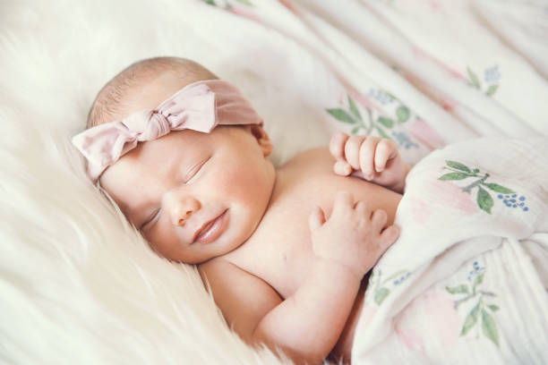 Sleeping newborn baby in a wrap on white blanket. Sleeping newborn baby in a wrap on white blanket. Beautiful portrait of little child girl 7 days, one week old. Baby smiling in a dream. baby girls stock pictures, royalty-free photos & images