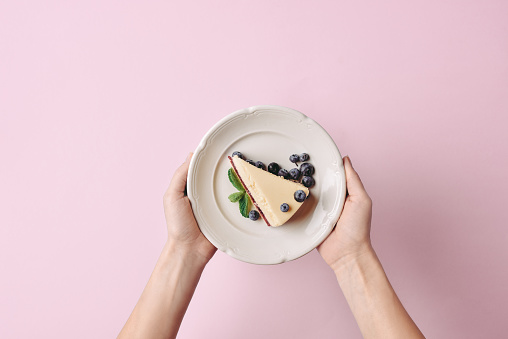 top view of woman holding slice of cheesecake with blueberries on plate