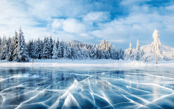 ghiaccio blu e crepe sulla superficie del ghiaccio. lago ghiacciato sotto un cielo blu in inverno. le colline dei pini. inverno. carpazi, ucraina, europa. - landscape colors cold horizontal foto e immagini stock