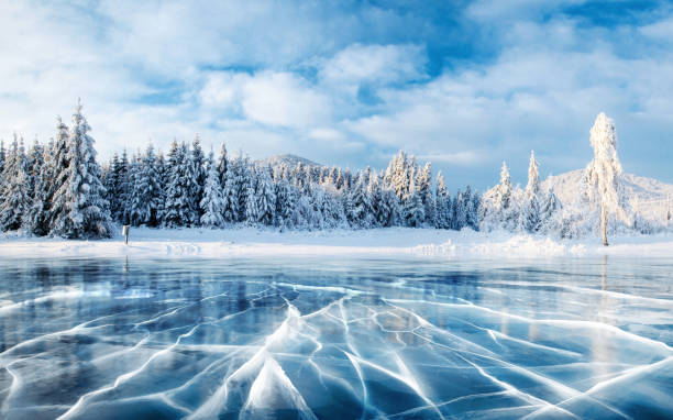 Blue ice and cracks on the surface of the ice. Frozen lake under a blue sky in the winter. The hills of pines. Winter. Carpathian, Ukraine, Europe. stock photo
