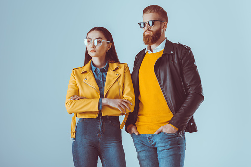 fashionable woman with arms crossed and bearded man in leather jackets isolated on blue