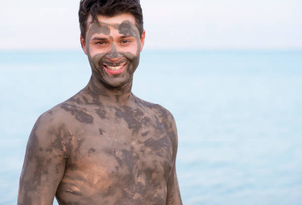 Portrait of handsome man with mineral mud of Dead Sea. Happy young man stained by the dirt of Dead Sea. people covered in mud stock pictures, royalty-free photos & images