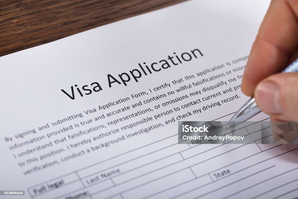 Person Filling Visa Application Form Close-up Of A Person Hand Filling Visa Application Form On Wooden Desk Passport Stamp Stock Photo