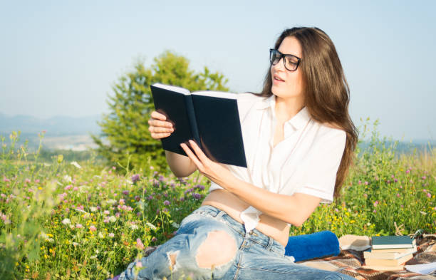 istock Pretty woman sitting on grass and reading book 853890994