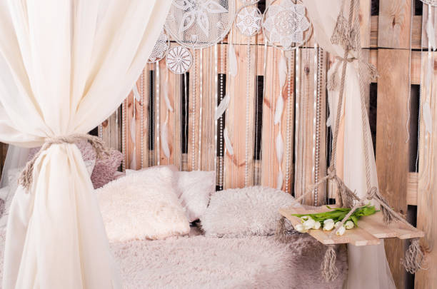 istock bed with soft pillows and the bed canopy swing with white tulips and white dream catcher with the white feathers and pearls hanging on a wooden background. 853893692