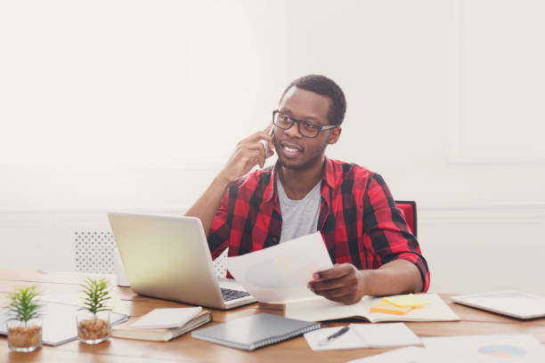 istock Young black businessman read documents and talk on mobile in modern white office 853899264