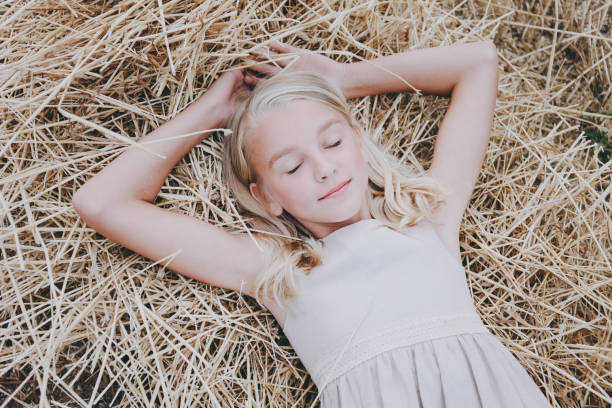 A beautiful cute girl lies on a hay with her eyes closed in a beige dress.