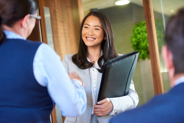 job candidate smiling as she enters the interview a young woman shakes hands with a recruitment manager as she enters the interview room College applicants stock pictures, royalty-free photos & images