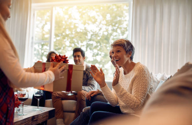 Little girl surprising her grandmother with a christmas present Little girl surprising her grandmother with a present for Christmas. Mature woman sitting with her family getting a christmas gift from granddaughter. multi generation family christmas stock pictures, royalty-free photos & images