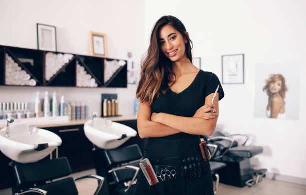 Female hairdresser standing in salon Female hairdresser in salon holding scissors in hand. Smiling young hairdresser standing in salon. beauty spa stock pictures, royalty-free photos & images